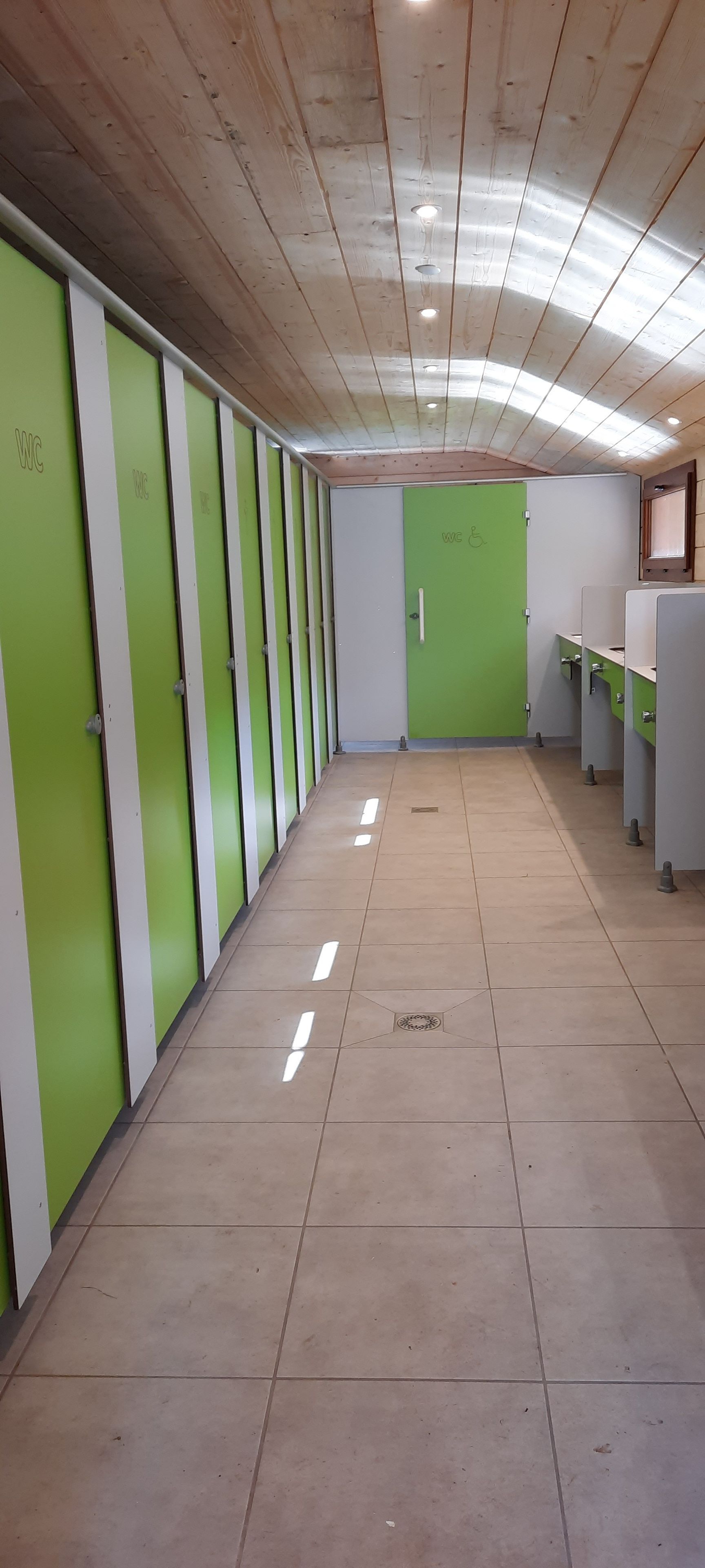 Een rij groene en witte kluisjes met een betegelde vloer en een plafond met inbouwverlichting.