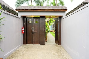 A gated entrance with a fire extinguisher on the left, a concrete pathway leading to a door with a small garden visible beyond. - Hill Retreat 3BR Pool Villa near Nai Harn, Rawai (Tambon Rawai)
