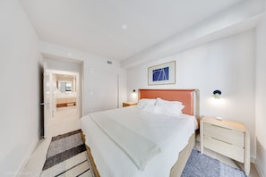 Habitació d'hotel moderna amb un llit gran, una tauleta de nit, un quadre al mur i una porta que dona a un bany.