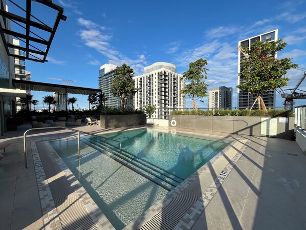 Zona de piscina al terrat amb vista despejada a edificis alts, cadiretas de relax i una torre de socorristers.