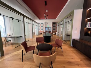 Un espai d'oficina modern amb parets de vidre, una taula rodona central i cadires, i un sostre vermell.