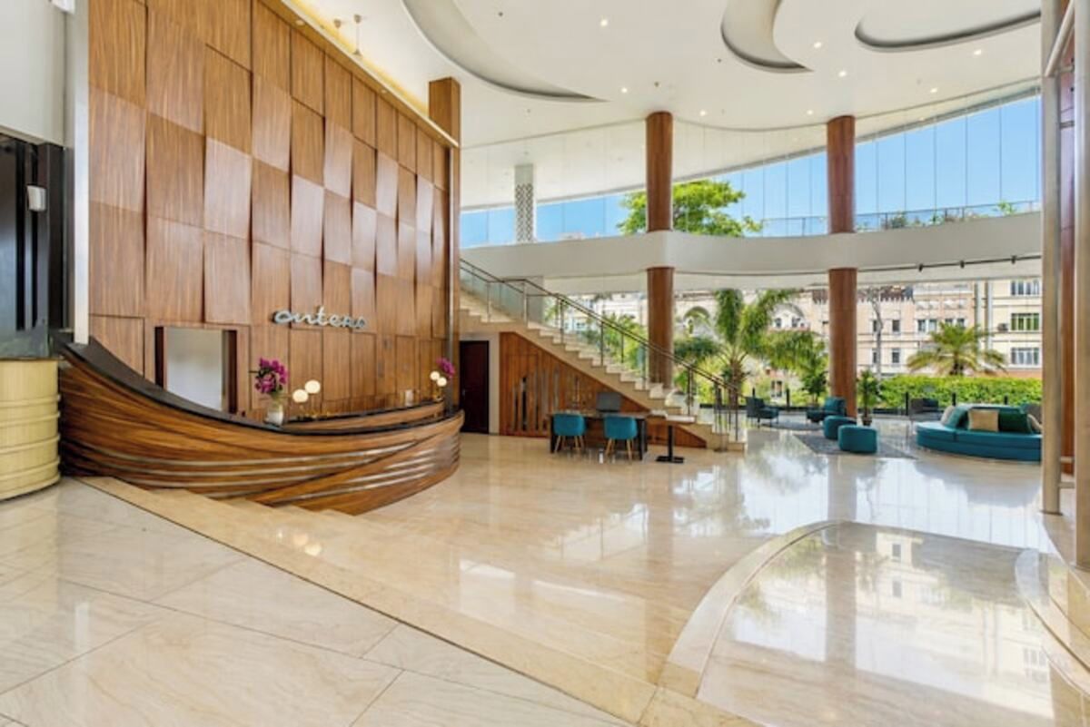 Un vestíbulo de hotel con una recepción, una escalera y un área de descanso con sillas y sofás.