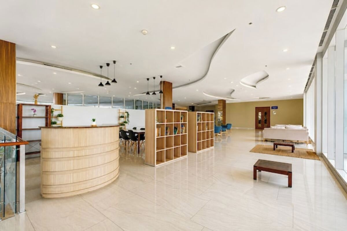 A modern hotel lobby with a curved reception desk, a seating area, and a large window providing natural light.