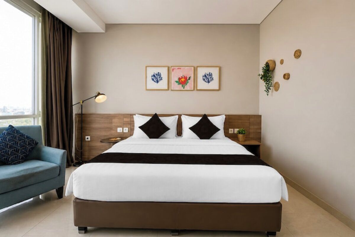 Una habitación de hotel con una cama, una mesita de noche, una lámpara, un sofá y un ventanal con cortinas.