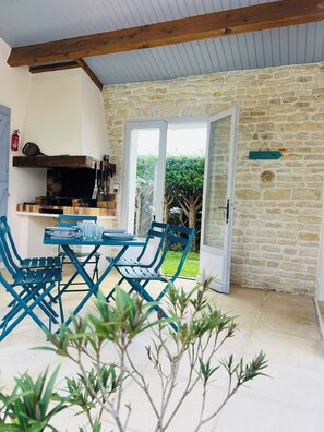 A dining area with a table and chairs, a stone wall, and a view of greenery outside. - New Listing (La Grève-sur-Mignon)