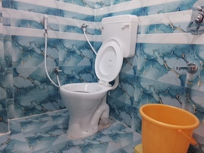 Une salle de bain avec des toilettes, une douche et un seau.