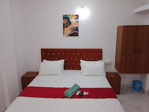Una habitación de hotel con una cama, dos mesitas de noche, una colcha roja y blanca, una obra de arte colorida en la pared y un armario de madera.