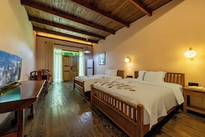 Een hotelkamer met een houten plafond, een bed met bloemenbedrukking, een bureau met een computer en een schilderij aan de muur.