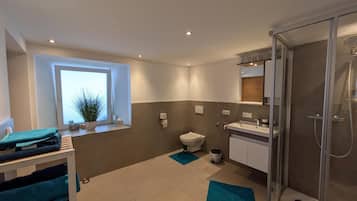 A modern bathroom with a toilet, sink, shower, and a window with a plant.