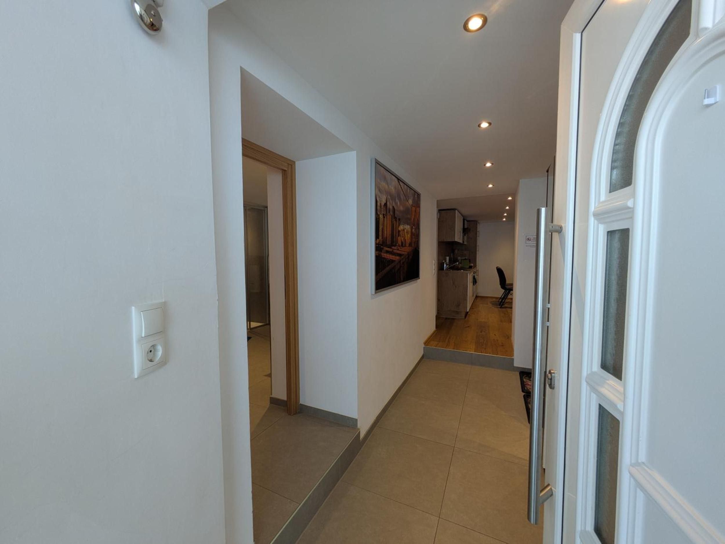 Un couloir avec une porte sur la droite, un tableau accroché au mur et, au fond, un espace cuisine.