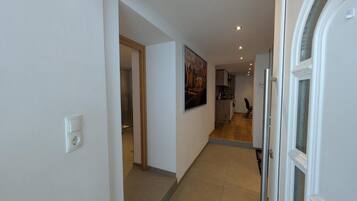 Un couloir avec une porte sur la droite, un tableau accroché au mur et, au fond, un espace cuisine.