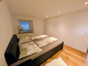 A bedroom with a bed, a window with a view, and a white rug. - Holiday Apartment 'Gurgltal' (Nassereith)