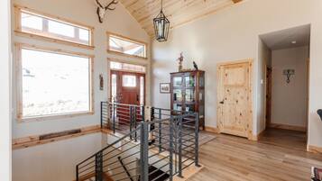 A spacious interior with a wooden staircase, large windows, and a rustic ceiling.