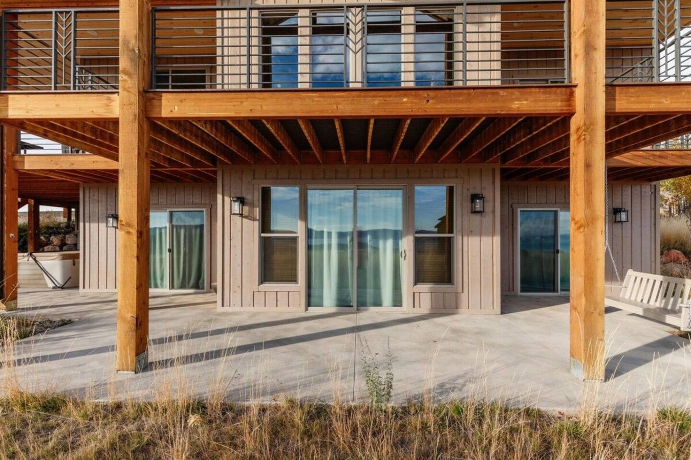 A wooden building with a covered patio, large sliding glass doors, and a bench.
