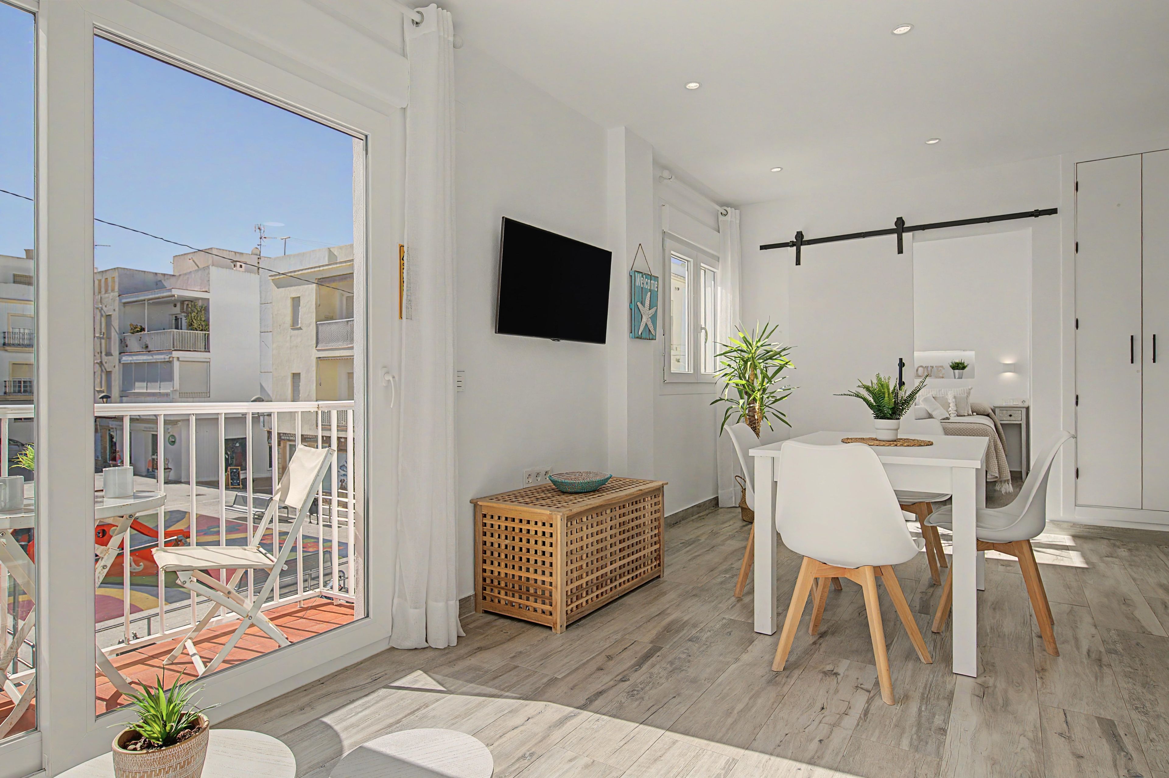 Un intérieur moderne comprenant un coin repas, un téléviseur fixé au mur et un balcon offrant une vue sur la ville.