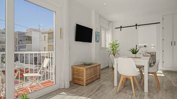 Un intérieur moderne comprenant un coin repas, un téléviseur fixé au mur et un balcon offrant une vue sur la ville.