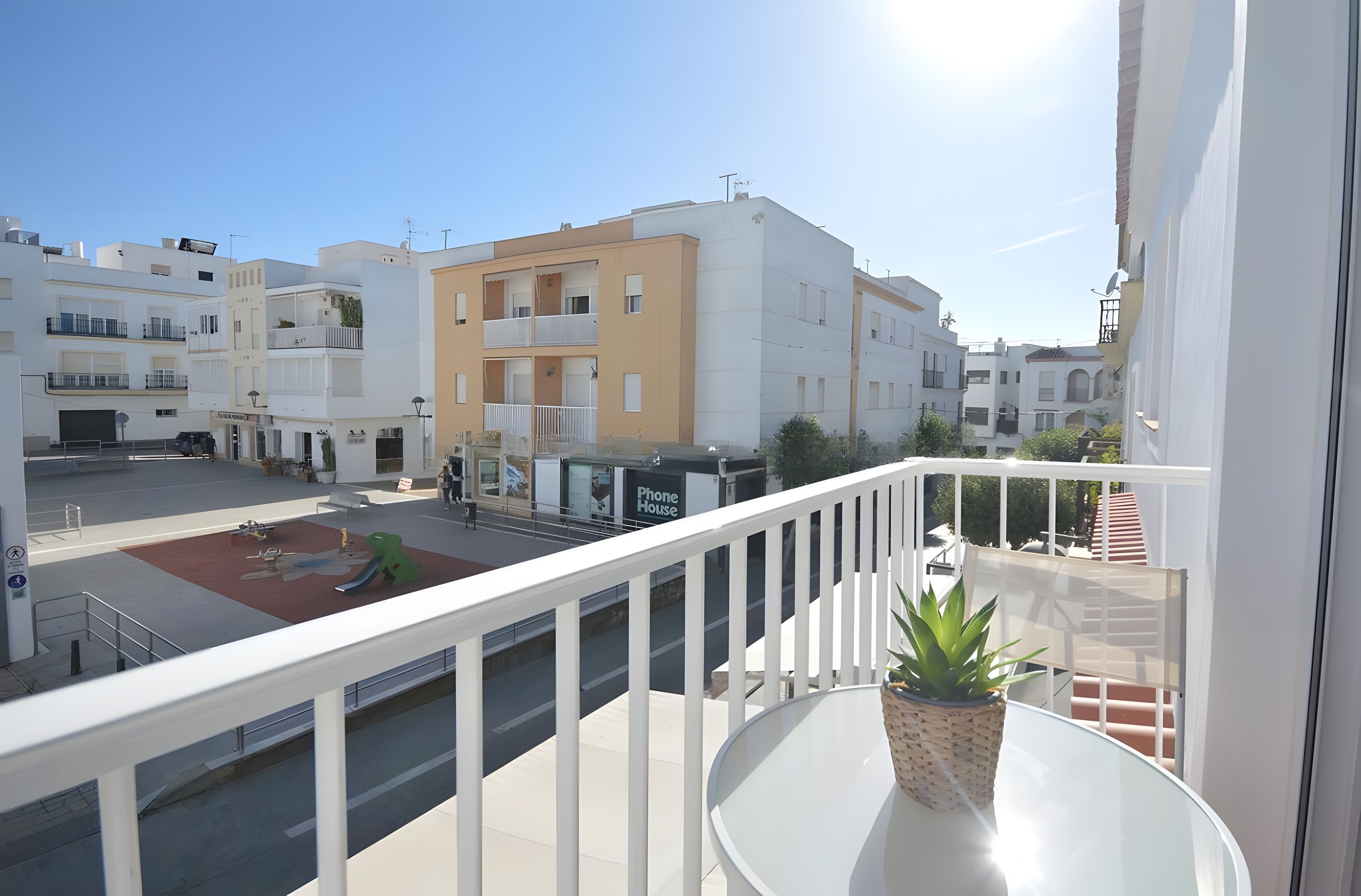 A balcony with a potted plant, a clear view of the street, and a building with a 'Phone House' sign.
