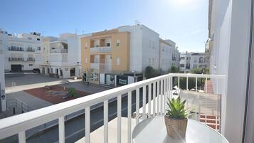 A balcony with a potted plant, a clear view of the street, and a building with a 'Phone House' sign.
