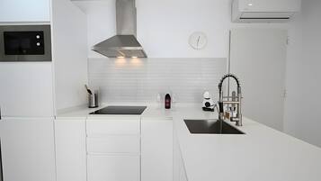 A modern kitchen with white cabinetry, a stainless steel range hood, a built-in oven, a double sink, and a wall-mounted clock.
