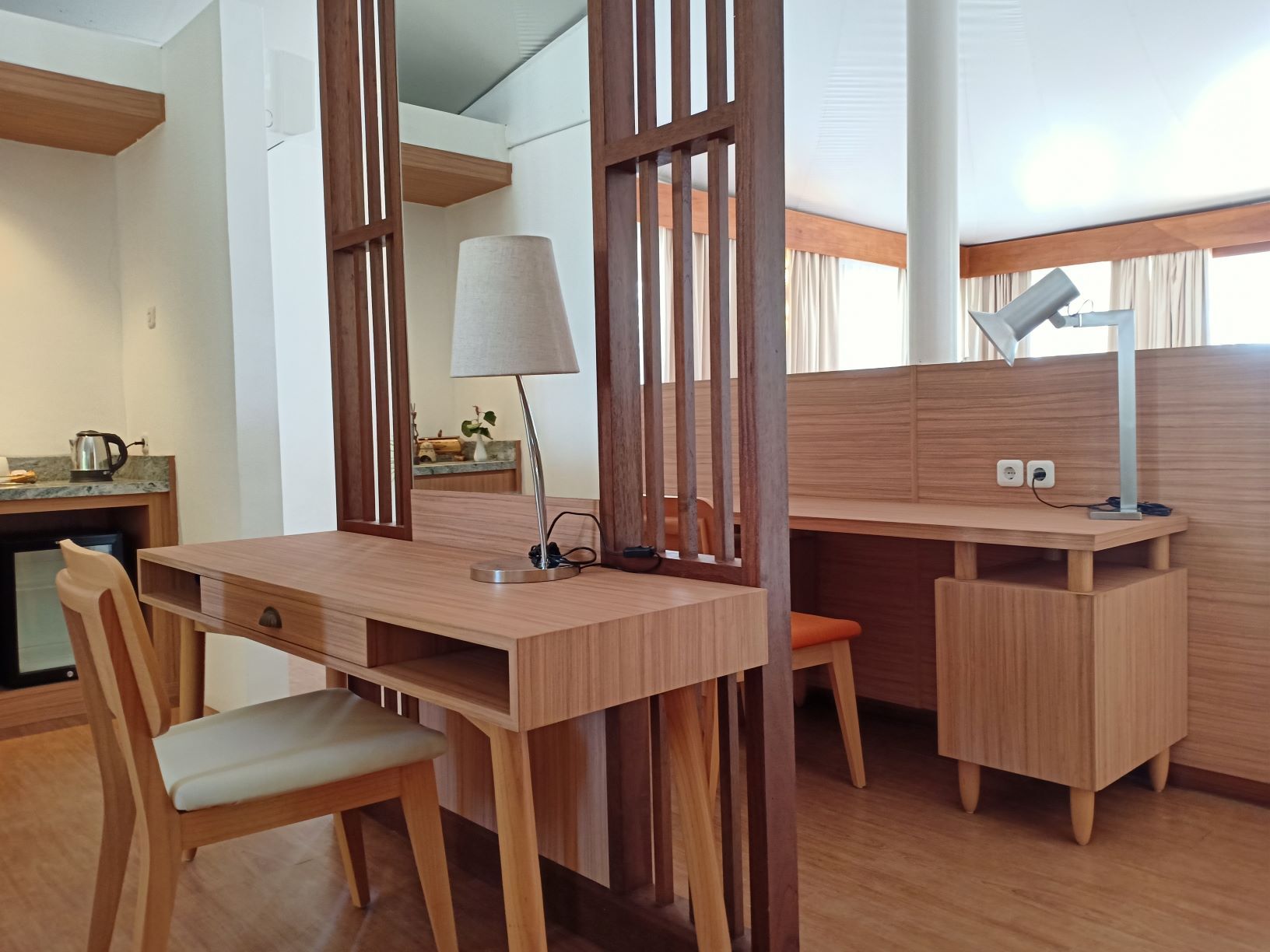 Una habitación moderna con un escritorio de madera, una silla, una lámpara y una pequeña mesa.