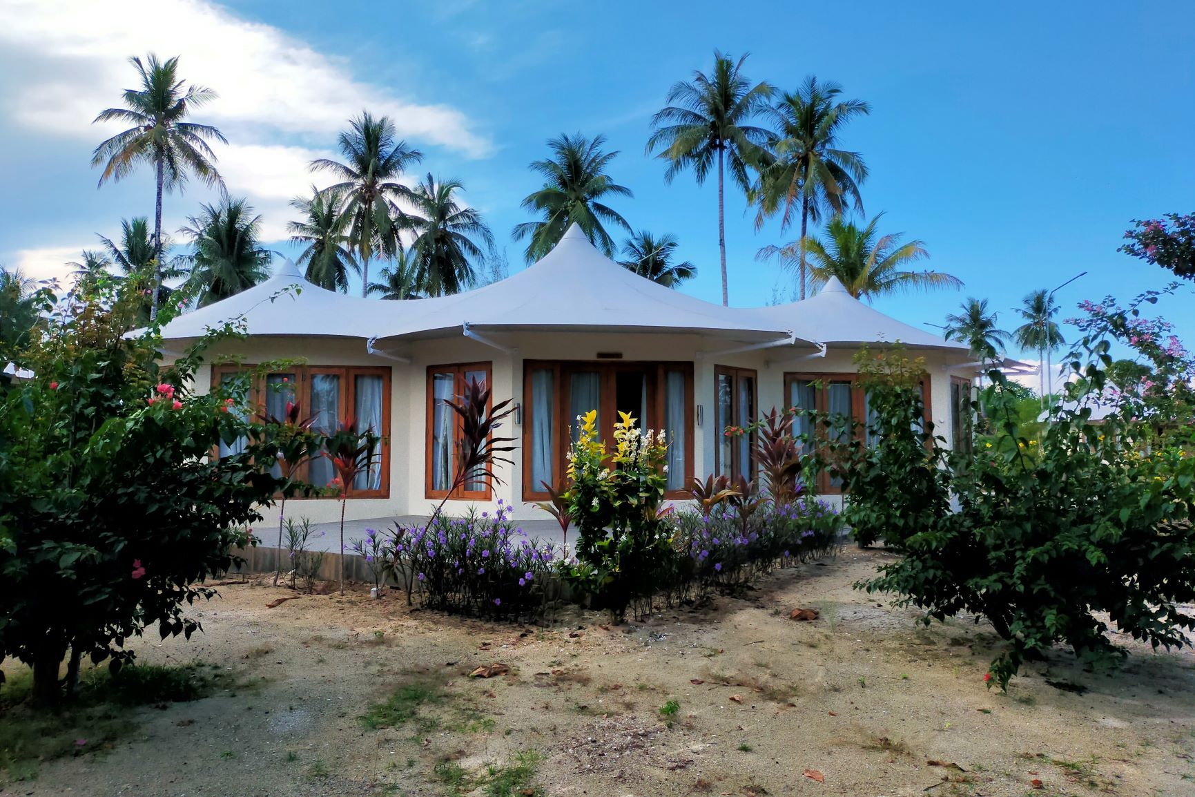 Un edificio de dos pisos con fachada blanca y marcos de ventana marrones, rodeado de follaje tropical y palmeras.