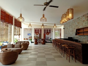 Amplia sala de estar con piso a cuadros, muebles de mimbre y una zona de bar con taburetes.