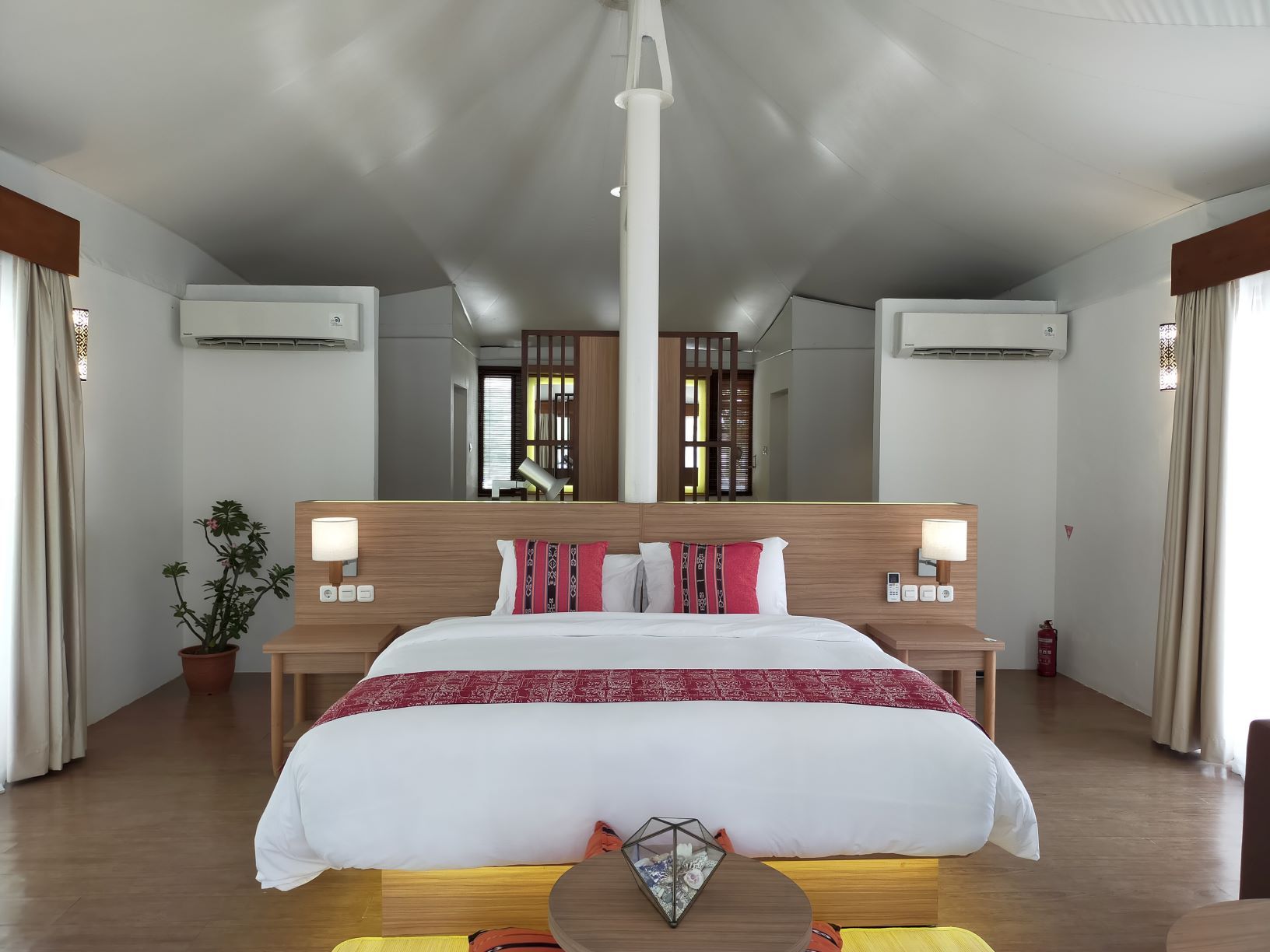 Una habitación de hotel con una cama grande, mesitas de noche, un espejo y un equipo de aire acondicionado.