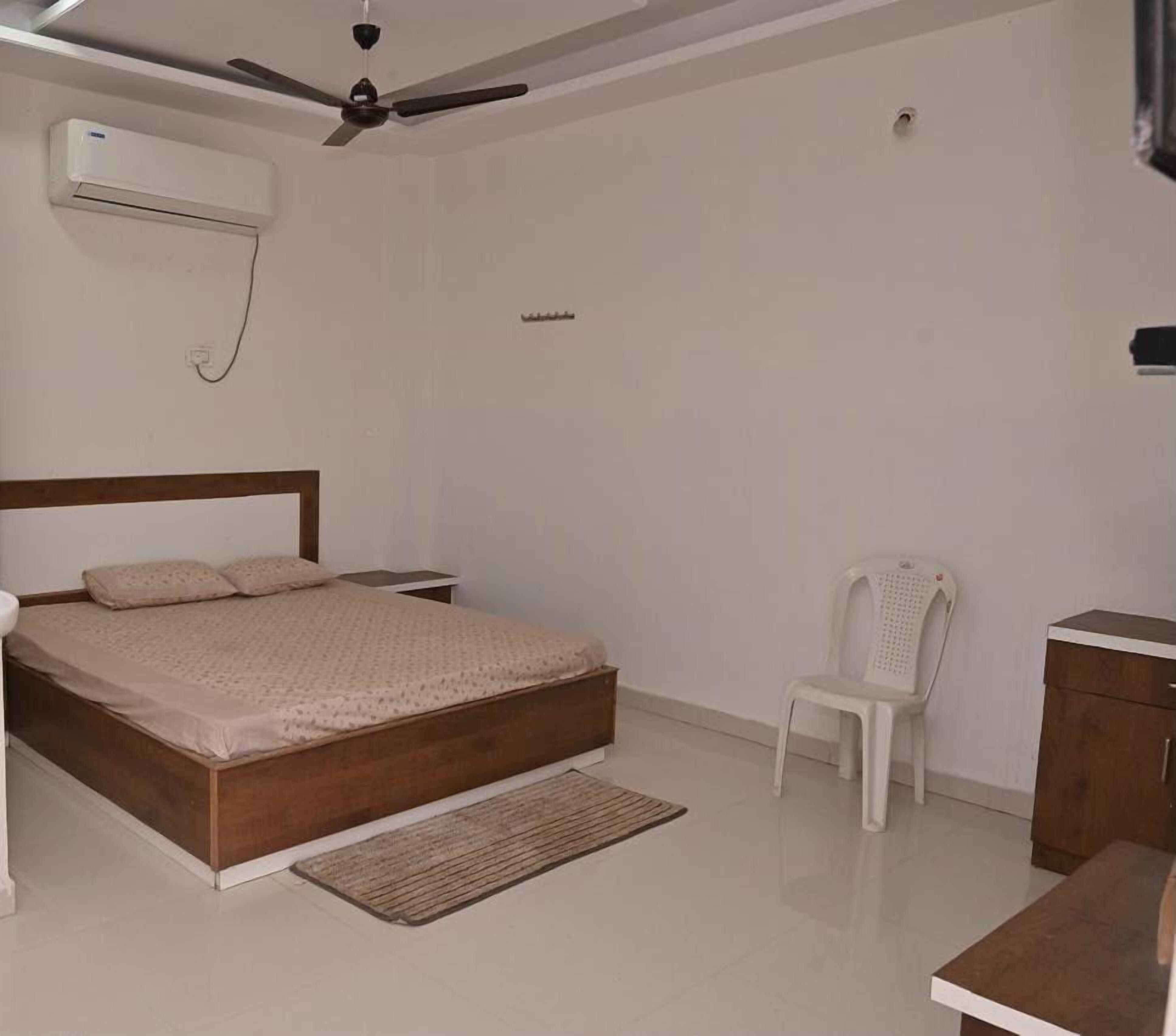 A bedroom with a wooden bed, a white chair, a small table, and a ceiling fan.