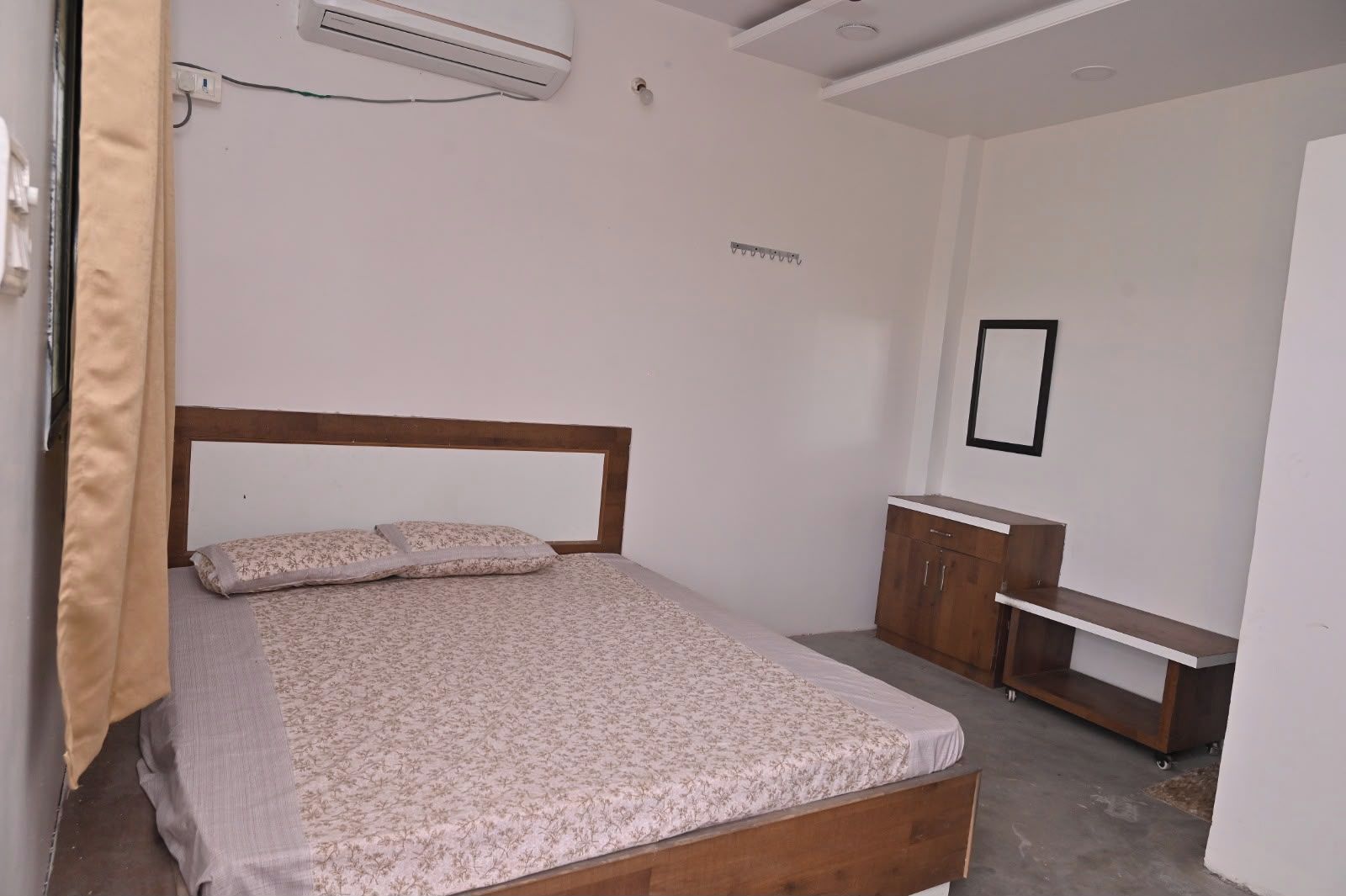 Une chambre à coucher avec un lit en bois, une table de chevet, un petit bureau et un appareil de climatisation fixé au mur.