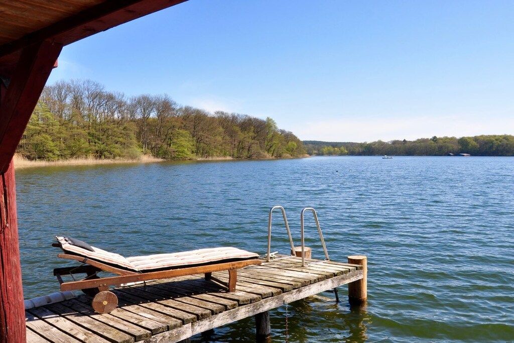 A wooden dock extending into a lake with a lounge chair and metal ladder.