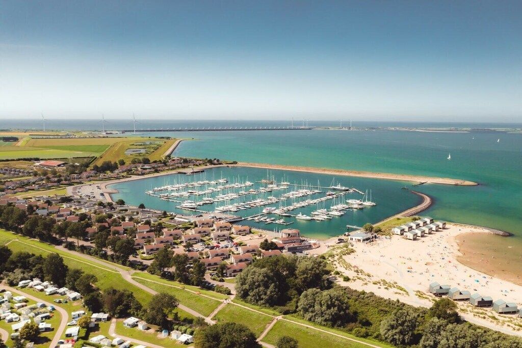 Ein Yachthafen mit zahlreichen Booten, ein Strandabschnitt mit Strandhäusern und ein Wohngebiet mit Häusern und Wohnwagen.