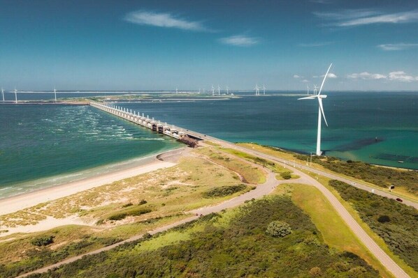 A coastal area with a long pier extending into the sea, surrounded by greenery and a clear sky.