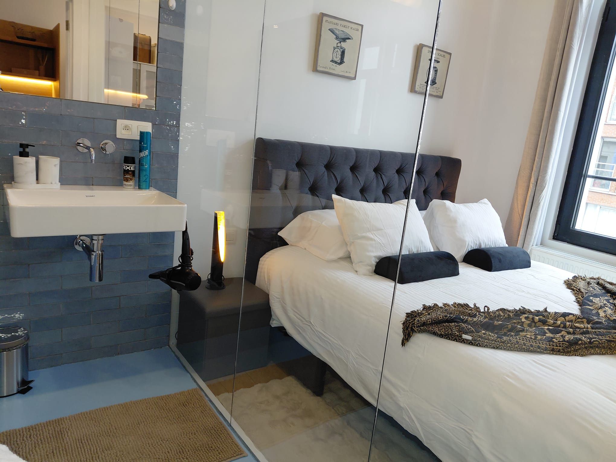 A modern bedroom with a large bed, a bedside table, a mirror, and a window.