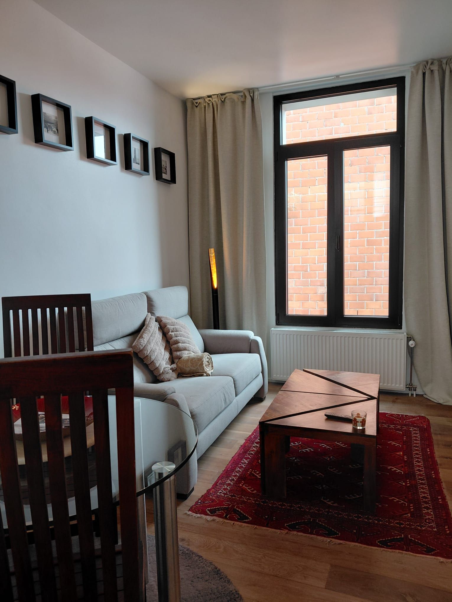 A living room with a sofa, a coffee table, a red rug, a fireplace, and a window with curtains.