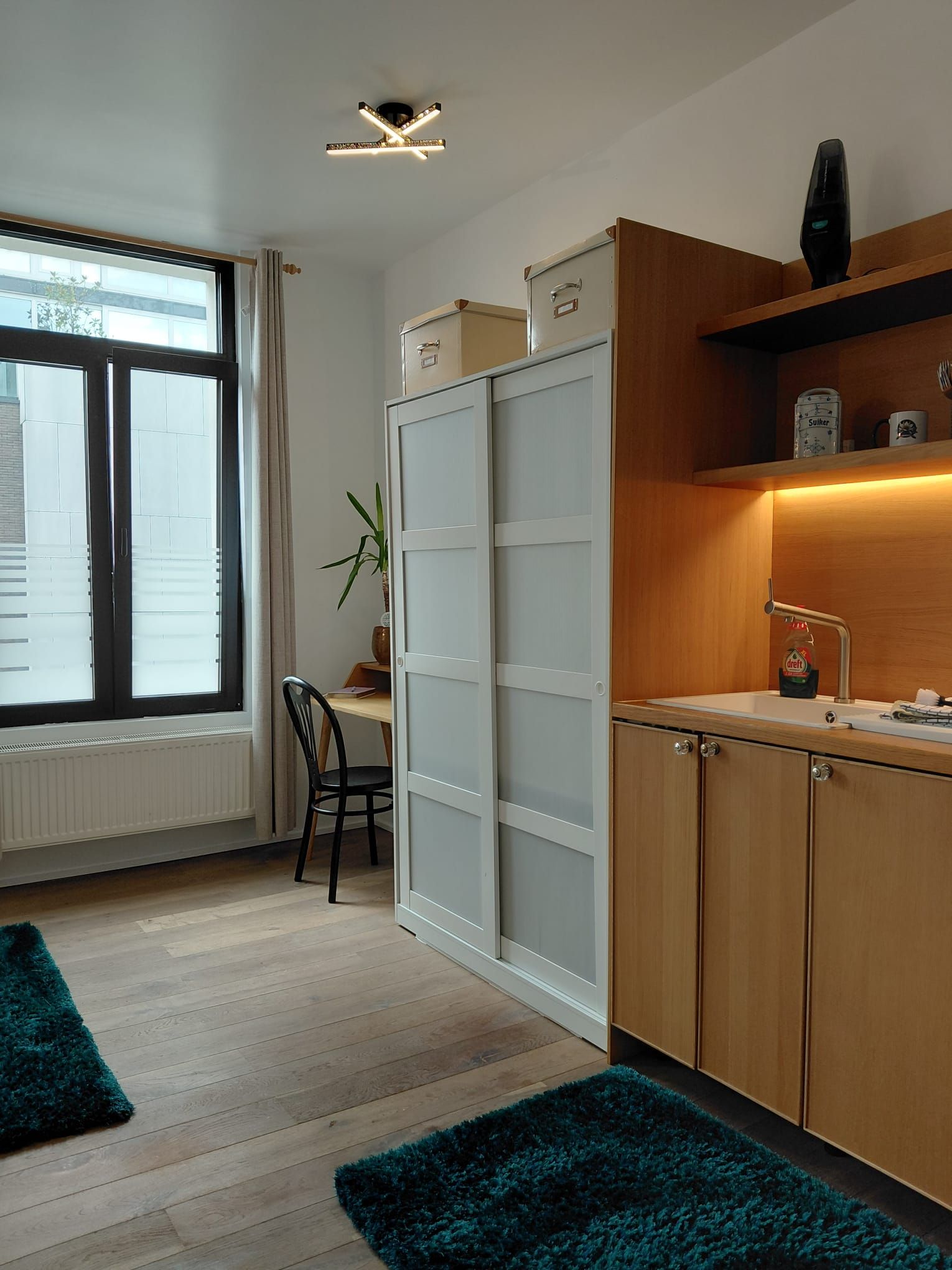 A modern kitchen with a sliding door, a dining area with a chair, and a view through a window.