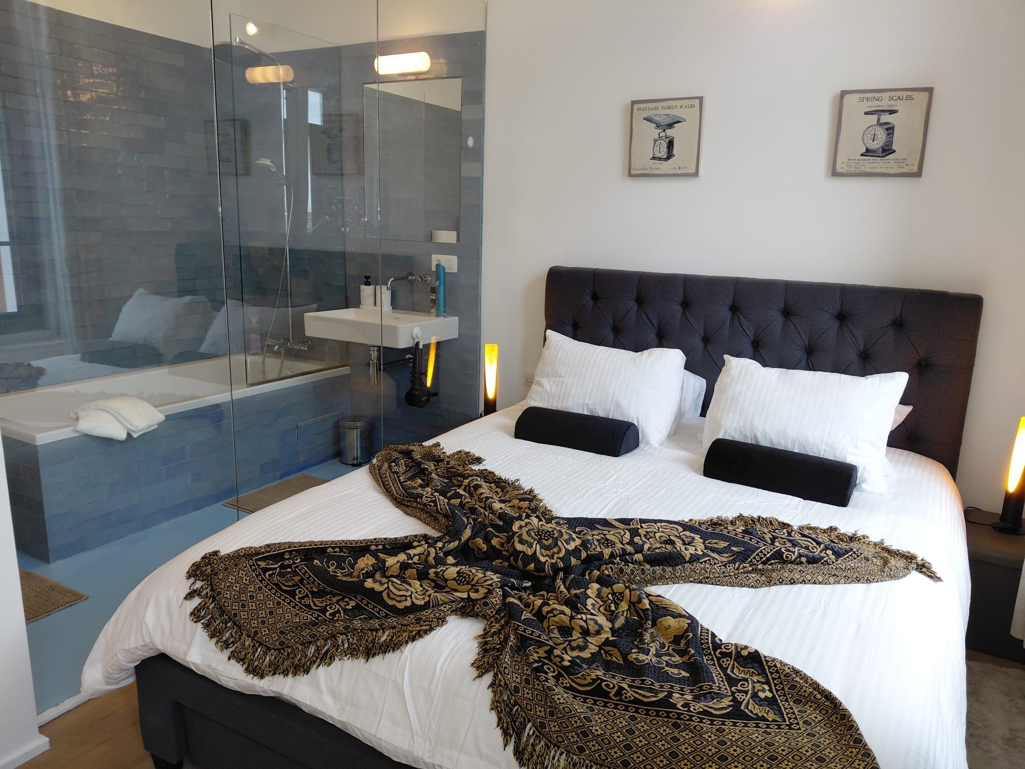 A bedroom with a large bed, a glass-enclosed shower, and two framed pictures on the wall.
