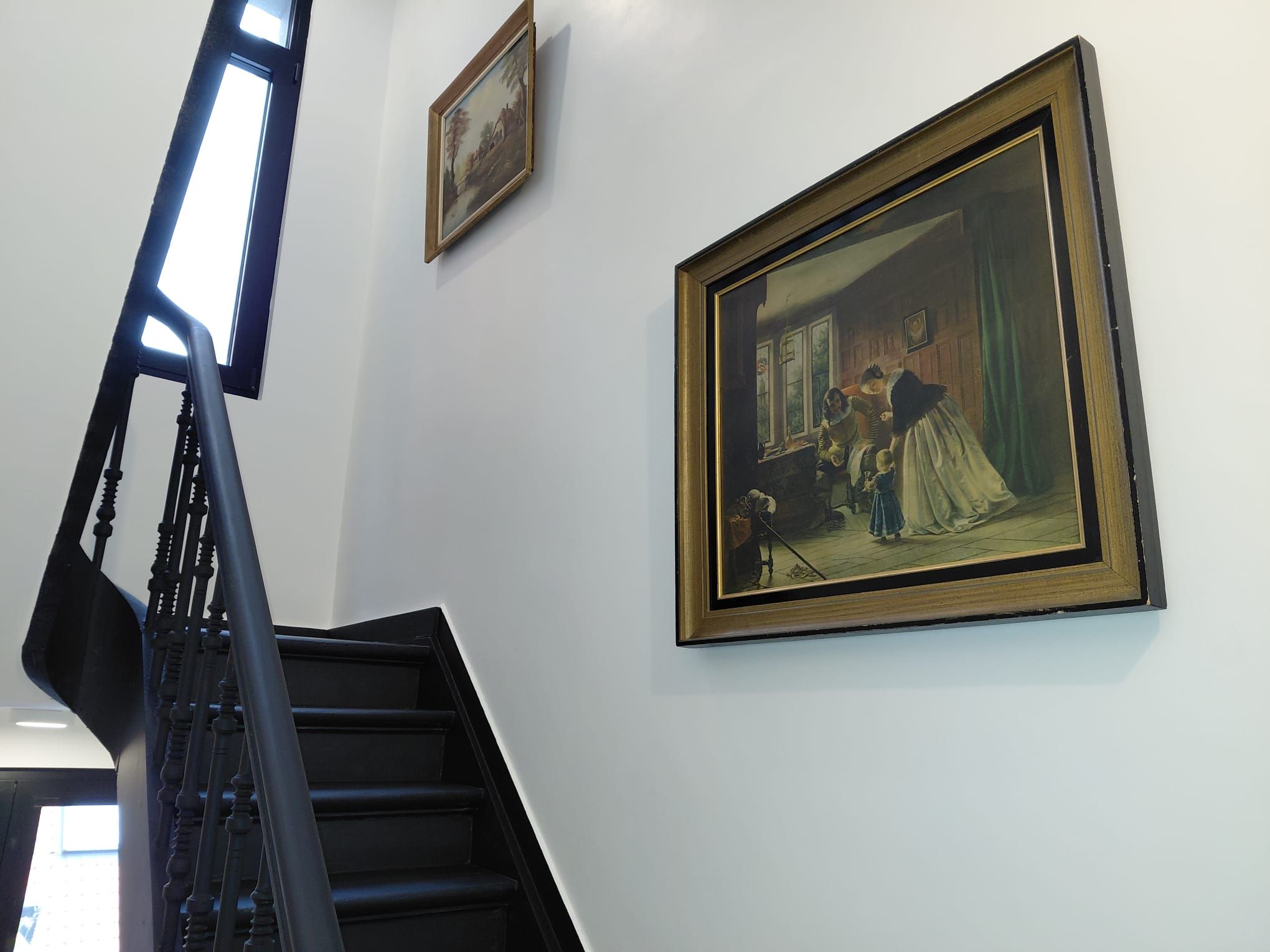 A staircase with a handrail and a painting of a domestic scene on the wall.