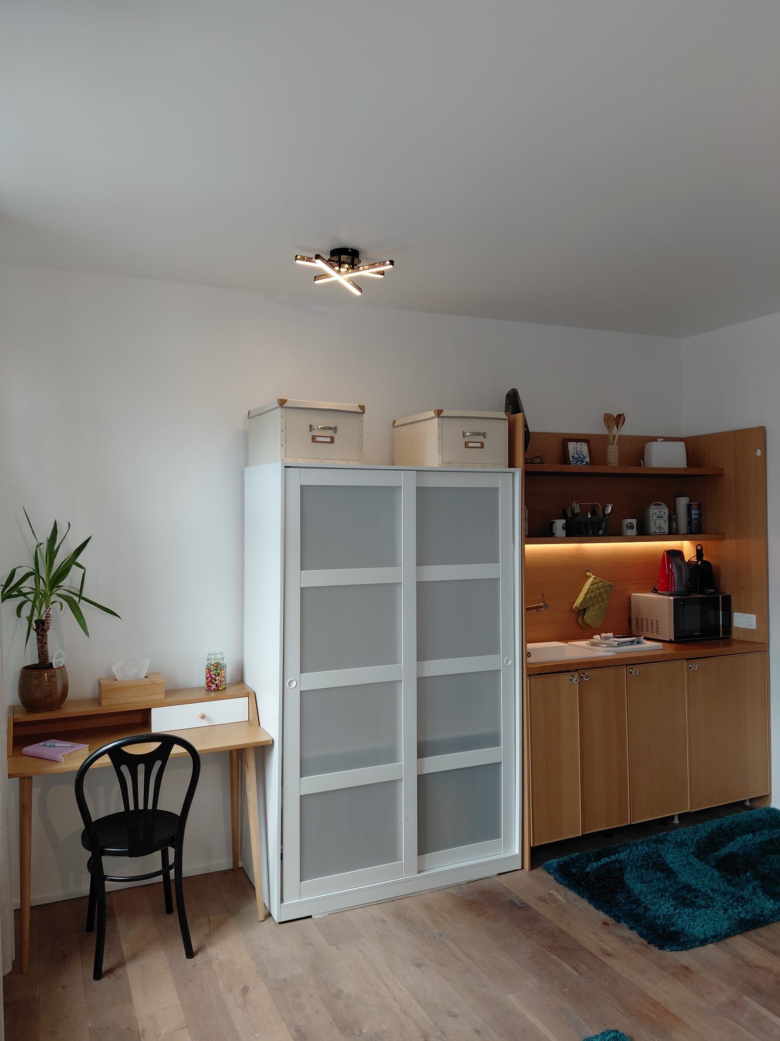 A compact kitchen with a white cabinet, a wooden countertop, and a black chair.