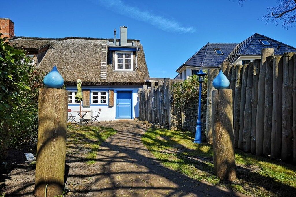 Ein traditionelles Haus mit einem Strohdach, einer blauen Tür und einem Holzzaun mit blauen Polern.
