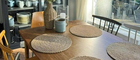 Spisebord med vævede bordskåner, en vase med grønne planter og en hængende lampe.