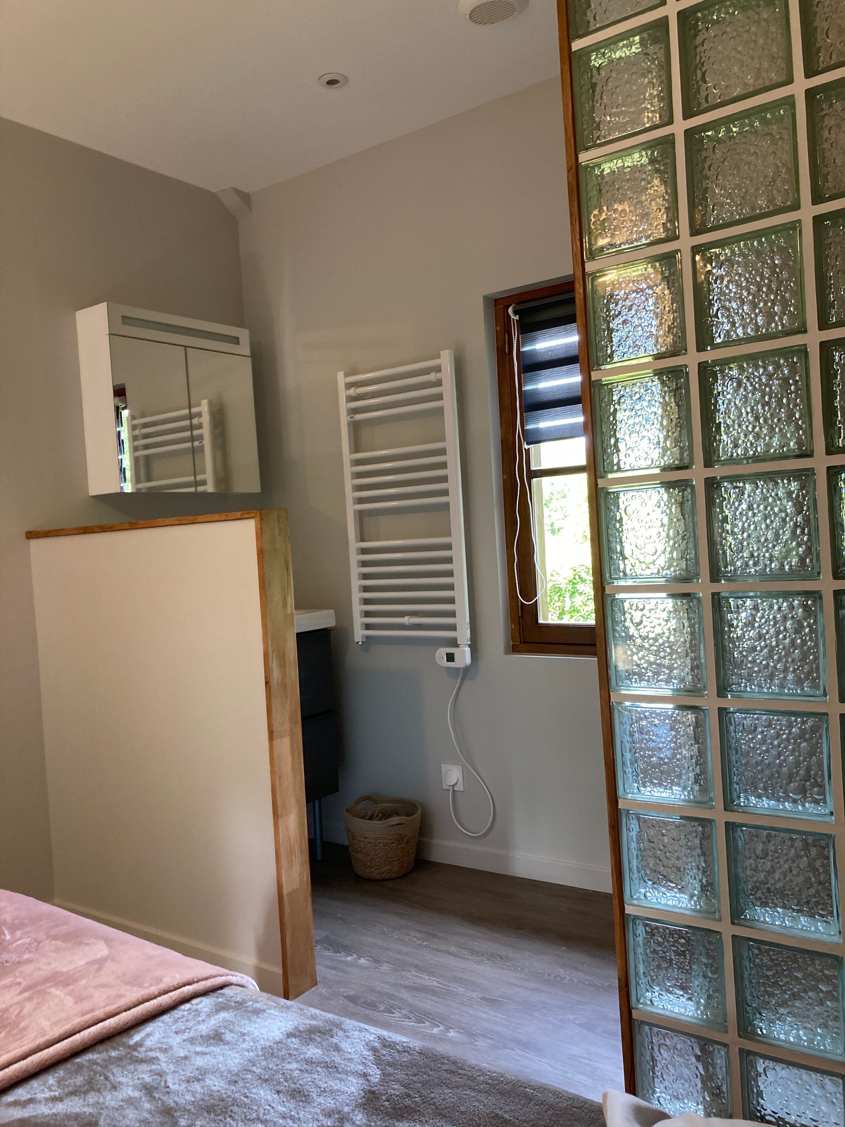 Ein Schlafzimmer mit einem Bett, einem weißen Heizkörper, einem Fenster mit Jalousien und einem an der Wand befestigten Spiegel.