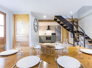 Una cocina moderna con horno empotrado, refrigerador y comedor con una mesa de madera lista para una comida.
