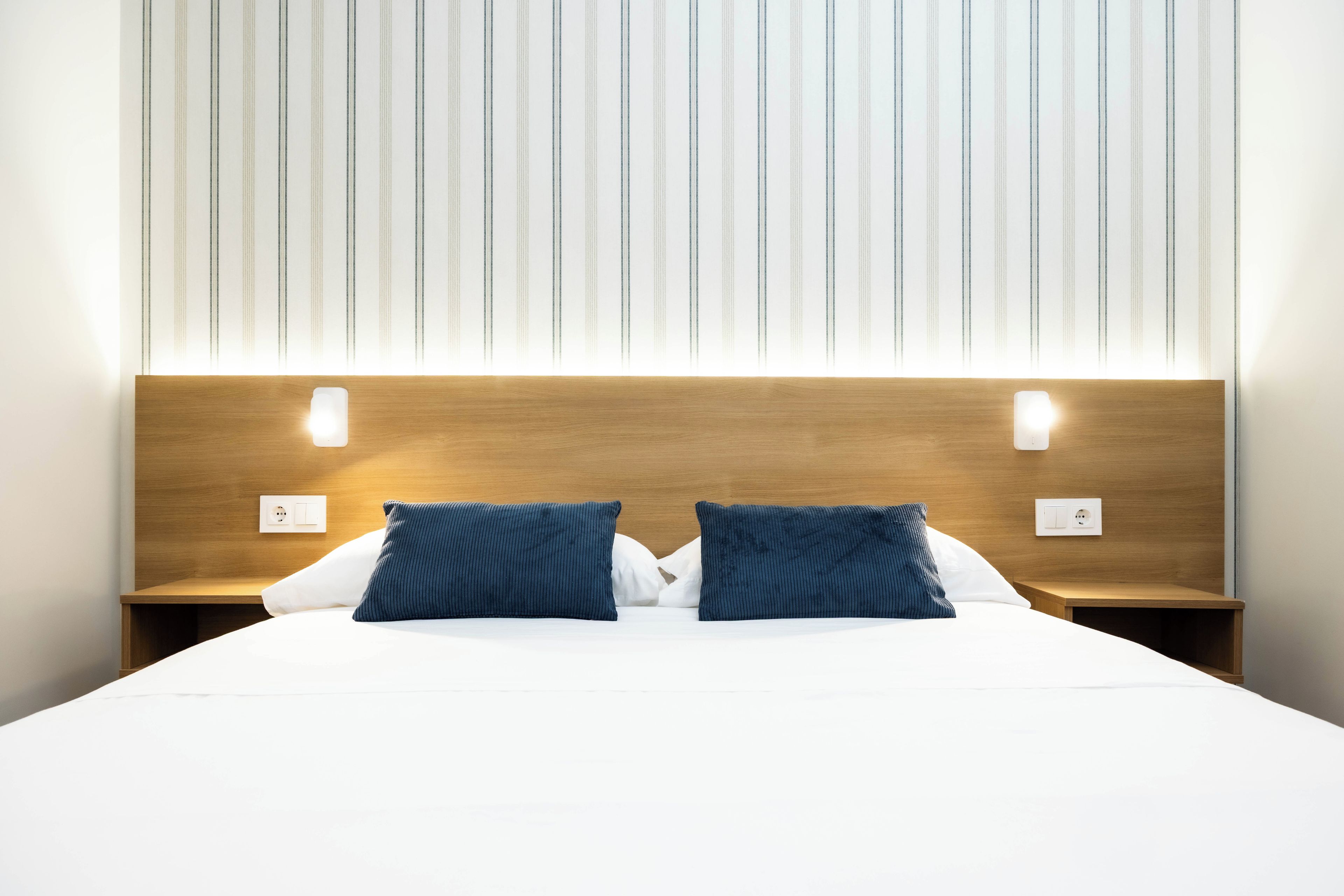 Quarto de hotel com uma cama grande, duas mesas de cabeceira e cabeceira de madeira.