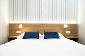 Habitació d'hotel amb un llit gran, dues taules de nit i un panell de fusta al capçal.