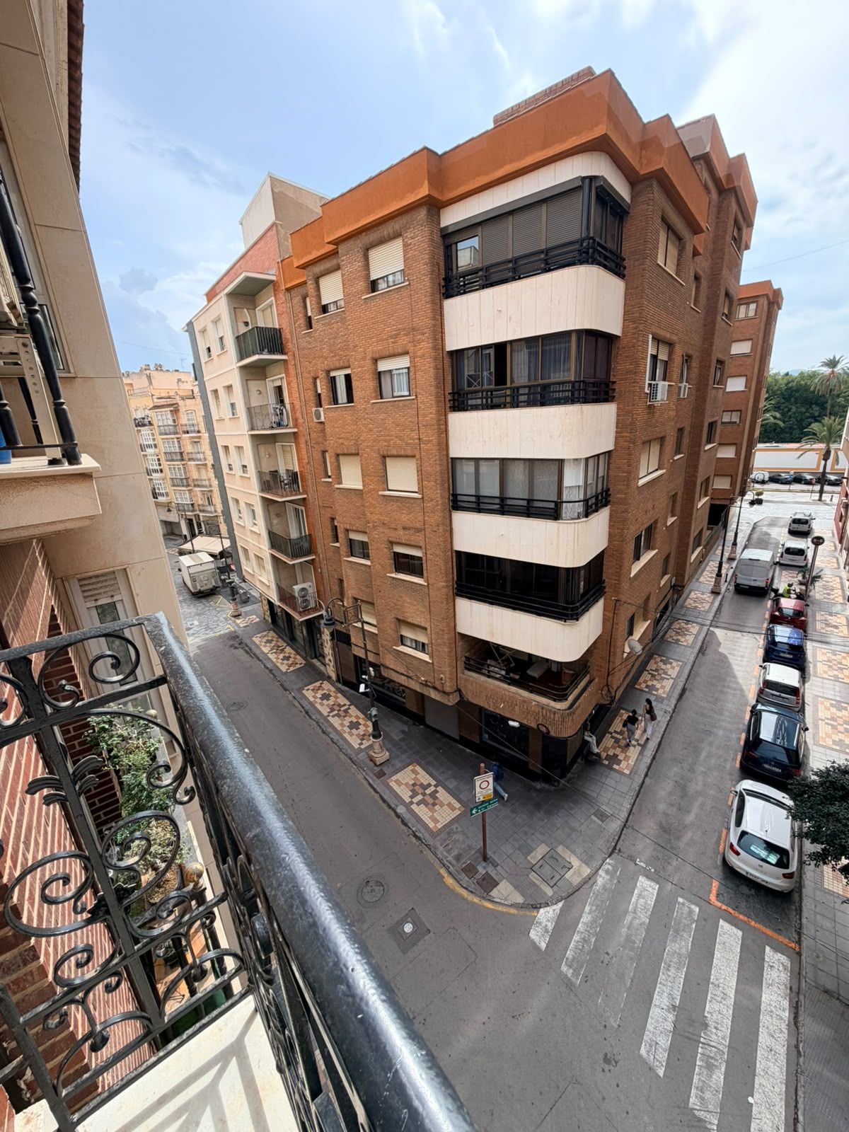 Un edificio residencial de varios pisos con balcones, un estacionamiento y un paso de peatones.