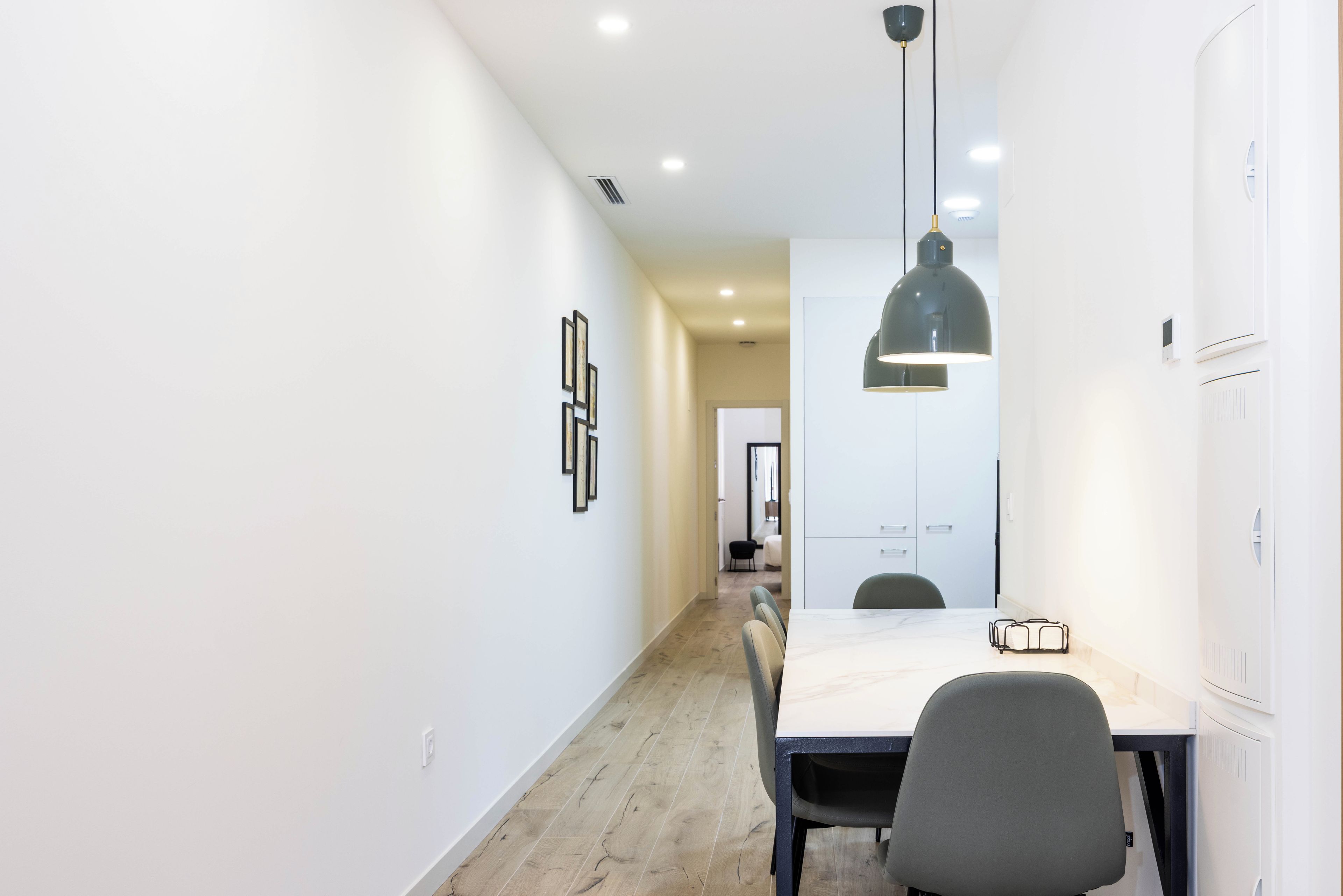 Un intérieur moderne comprenant un espace repas avec une table et des chaises, un luminaire suspendu et un couloir menant à une pièce dotée d’une porte.