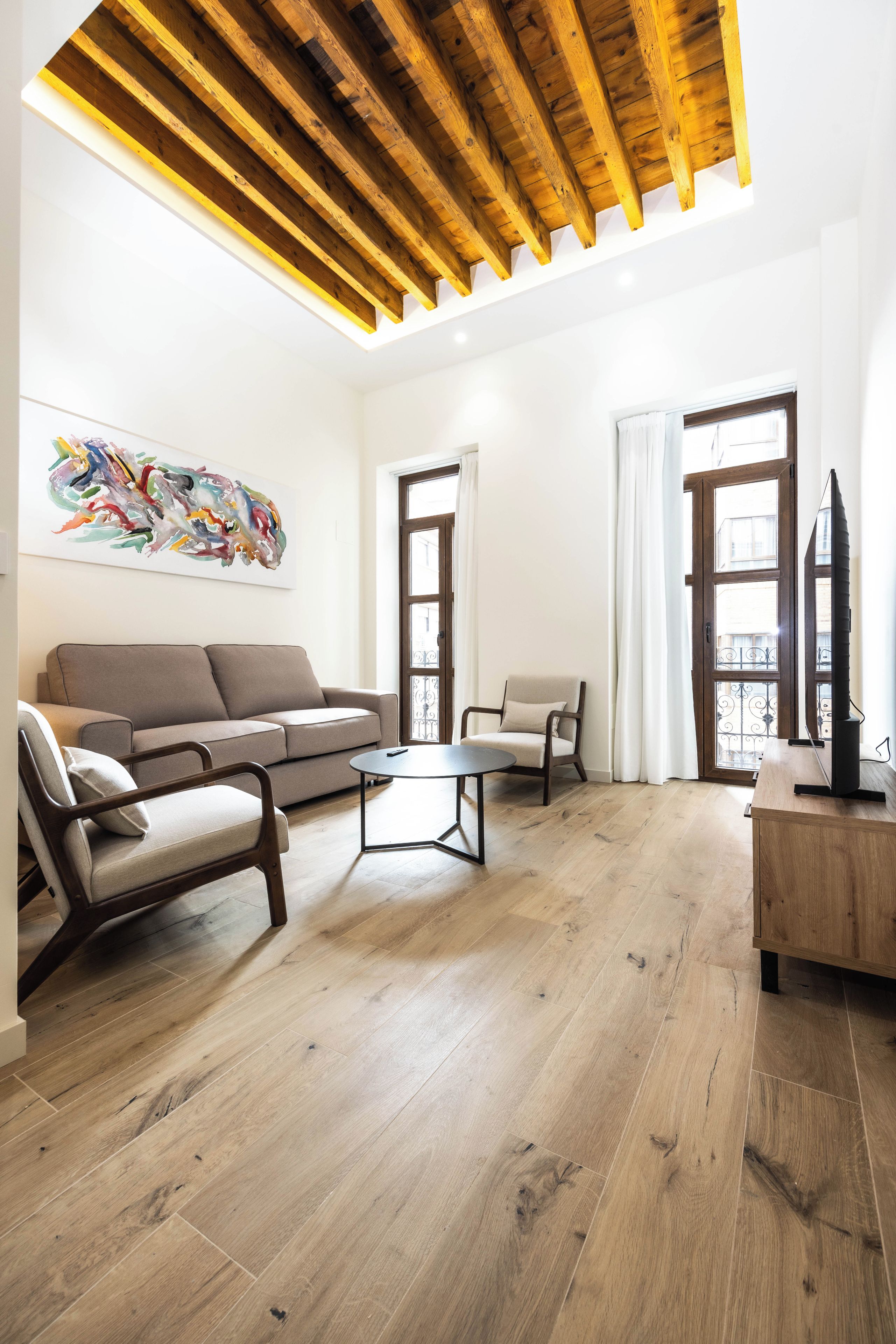 A modern living room with a wooden ceiling, a sofa, a chair, a coffee table, and a TV on a wooden stand.