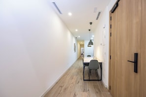 Un passadís amb una porta de fusta, una taula de dinar amb cadires i il·luminació encastrada al sostre.