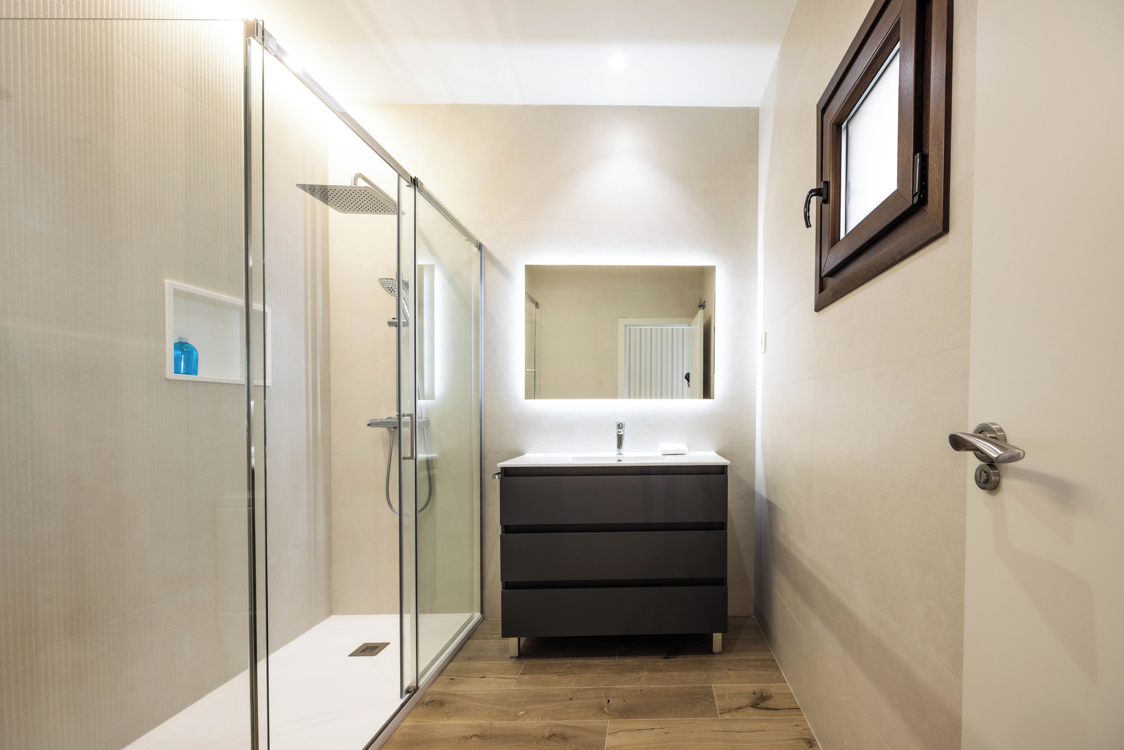 A modern bathroom with a glass shower enclosure, a vanity with a mirror, and a wooden floor.