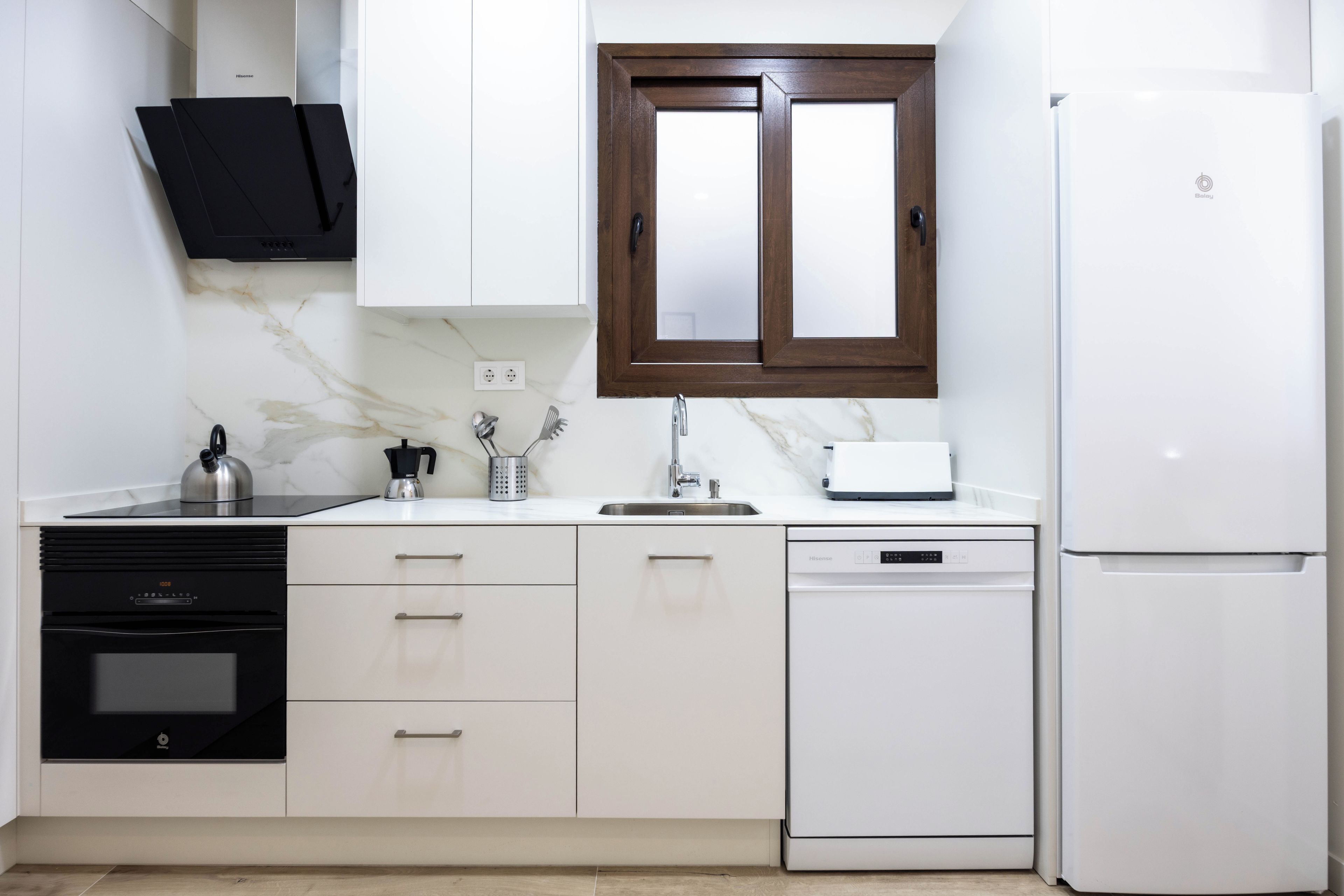 Una cocina moderna con armarios blancos, un lavavajillas negro, un refrigerador blanco y un gabinete de madera sobre el fregadero.